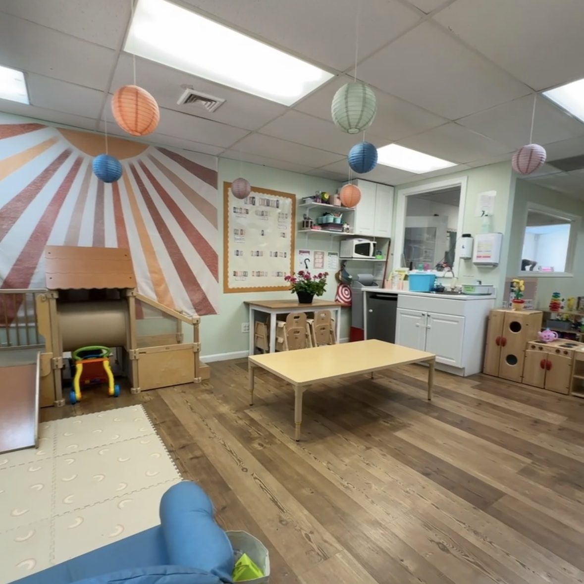 Photo of Waddler classroom with slide, table padded rug, and decorations on the walls.