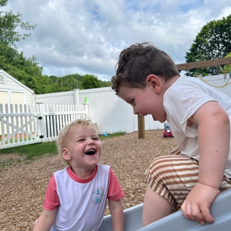 Two toddler boys laughing outside on the playground.