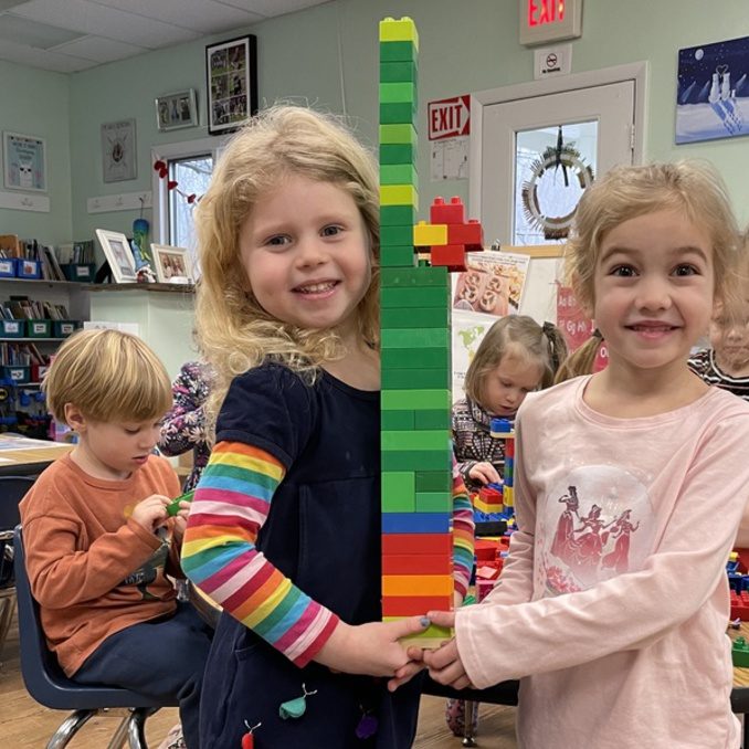 Two girls smiling holding a lego tower